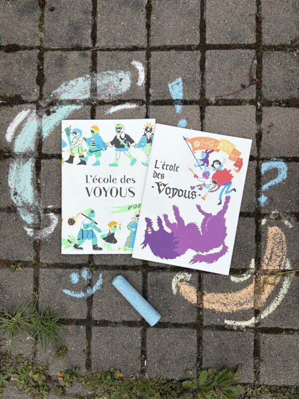 Photo des deux exemplaires du fanzine s'appelant l'école des voyous, l'un est vert et l'autre est violet. Le fond est un sol en béton avec des dessins à la craie, rappelant le côté enfantin de ce livre.