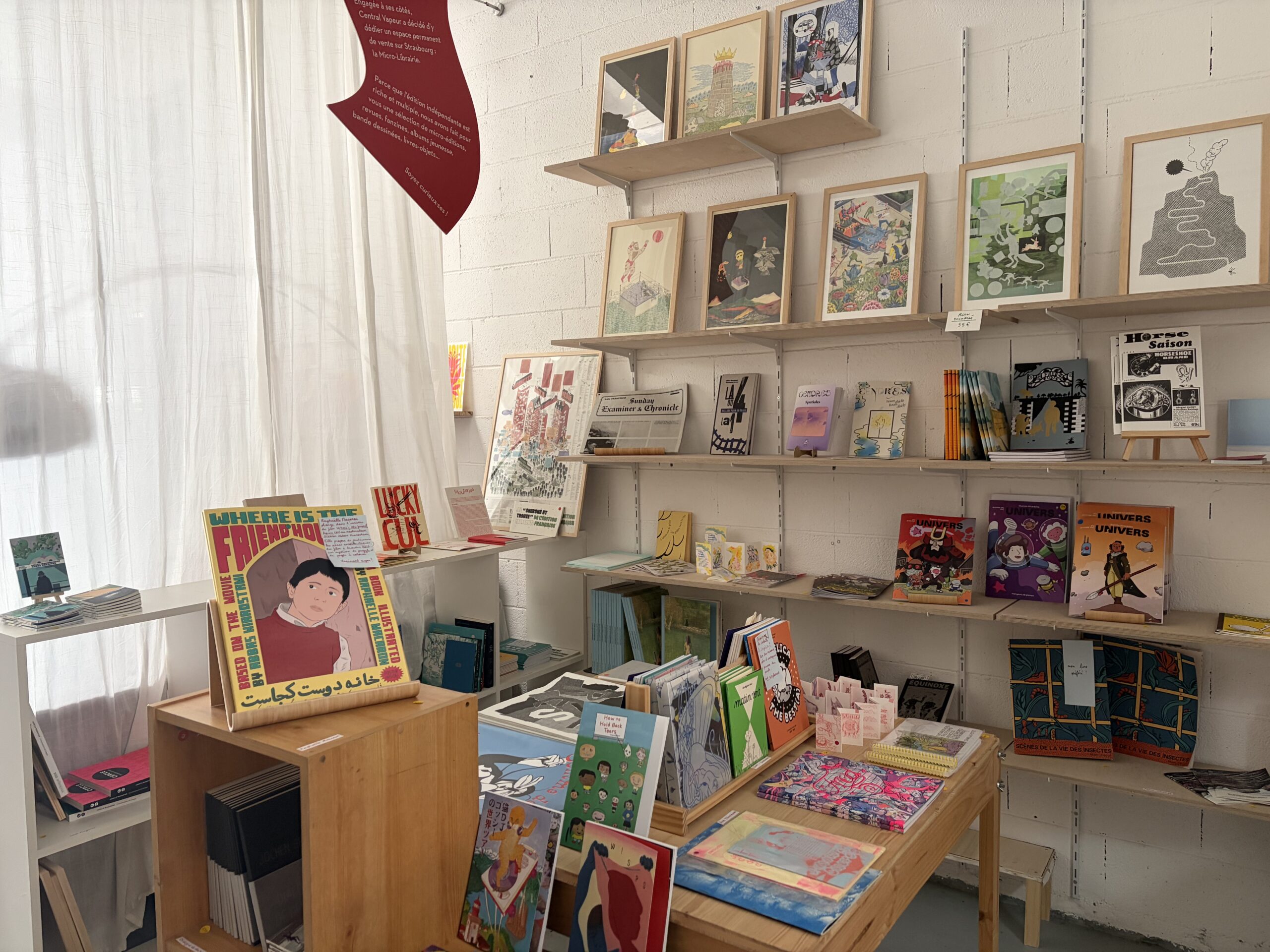 Photo d'ensemble de la micro-librairie, il y a une table centrale avec les nouveautés et des étagères